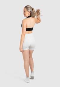 Zwarte sportbeha en witte hoge taille short, model van achteren. Haar in een paardenstaart, minimale details, soepel, rekbaar materiaal.