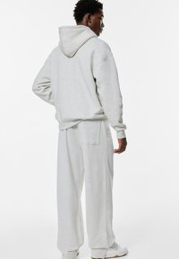 Lichtgrijze hoodie en bijpassende wijde sweatpants in een zachte textuur. Gewatteerd ontwerp met een achterzak en geribde manchetten.