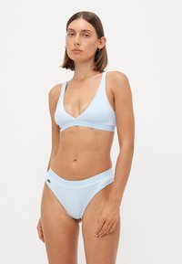Šviesiai mėlynas bikini komplektas, kuriame yra trikampio formos liemenėlė su plonomis petnešėlėmis ir derančios mažai pakeltos bikini kelnaitės, papuoštos mažu logotipu.