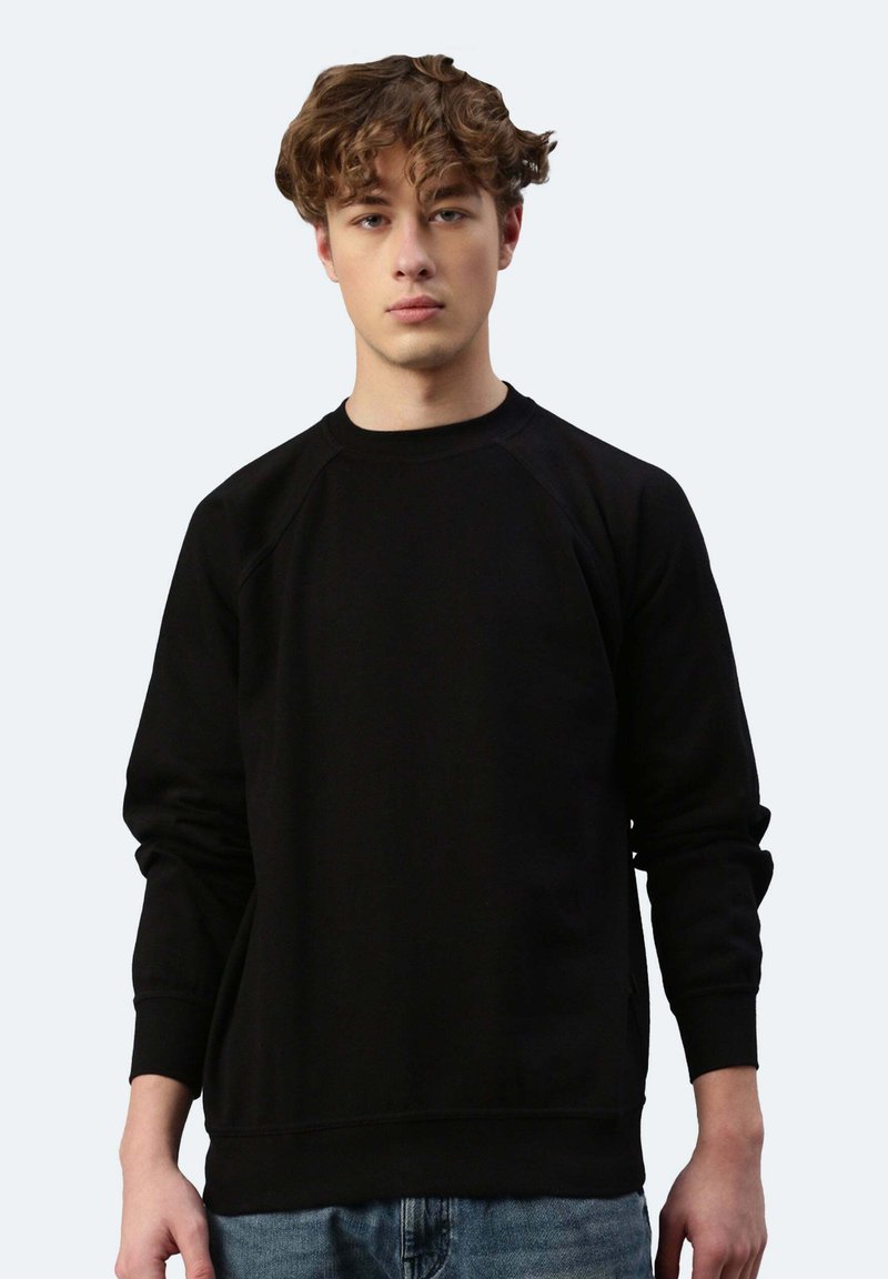 Felpa nera con maniche raglan, collo a giro e polsini a coste. Tessuto morbido; design minimale; indossata con jeans azzurri chiari.