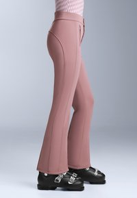 Ružične skijaške hlače po mjeri s raširenim nogavicama, s detaljima patentnog zatvarača i šavova, upari s crnim skijaškim čizmama s metalnim kopčama.