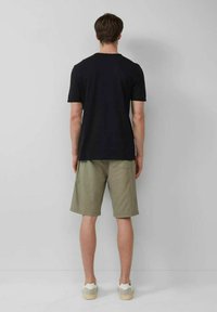 Black short-sleeve t-shirt, olive green shorts, and white sneakers, viewed from the back. Simple design, standard fit, cotton texture.