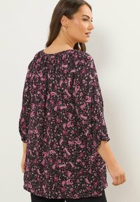 Tunic nera con motivo paisley rosa, maniche tre quarti, scollo elastico e vestibilità morbida. Tessuto morbido e leggero.
