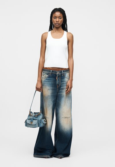 Γυναίκα με μακριά πλεξούδες που φοράει λευκή μπλούζα χωρίς μανίκια και φαρδιά ξεβαμμένα μπλε τζιν, κρατώντας μικρή μπλε τσάντα με αλυσίδα.