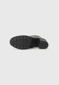 Black boot sole with a textured, rugged tread pattern for grip. Made of rubber, featuring a thick heel and sturdy design.
