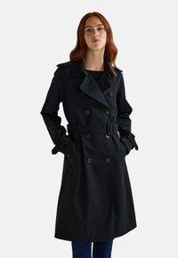 Trench-coat noir avec un design croisé, une ceinture à la taille et des poignets boutonnés, confectionné dans un tissu lisse et texturé.