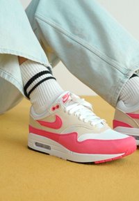 Os ténis Nike Air Max 1 apresentam um cabedal branco com realces em rosa, um swoosh texturizado e uma unidade de ar visível na sola. Sola preta.