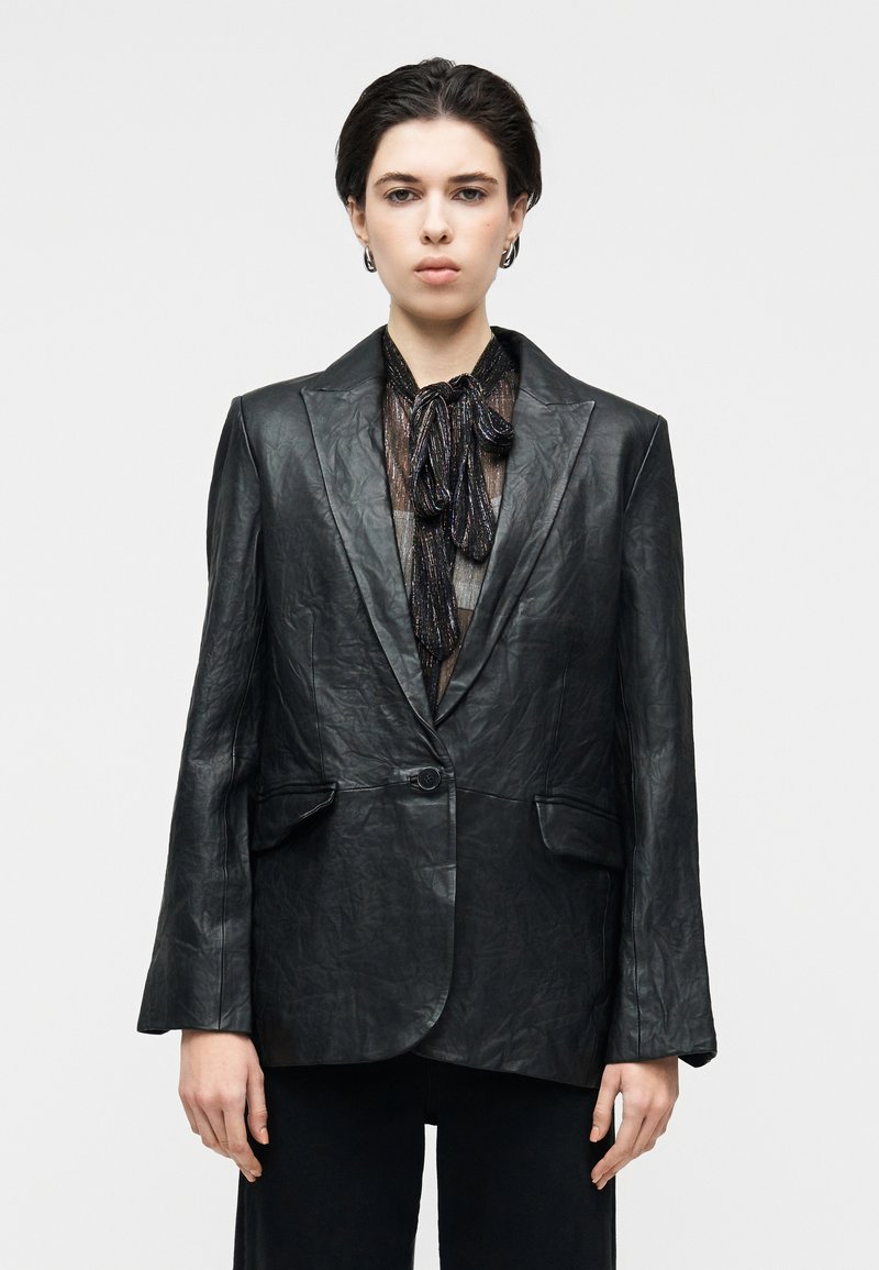 Μαύρο δερμάτινο σακάκι με δομημένη εφαρμογή, για κά σαλονιού, κλείσιμο με ένα κουμπί και δύο μπροστινές τσέπες. Υφή με ρυτίδες.