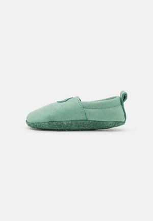 Grüne Slipper aus weichem Wildleder, mit einer strukturierten Filzsohle, runder Spitze und einer Schlaufe an der Rückseite für einfaches An- und Ausziehen.