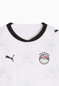 Maillot de football blanc avec col noir, logo Puma noir sur le côté droit de la poitrine, et emblème de la Fédération Égyptienne de Football avec cinq étoiles sur le côté gauche de la poitrine.