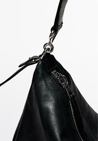 Sac à main en cuir noir avec fermeture éclair, matériel en argent et surface texturée. Sangle ajustable attachée par un anneau en métal.