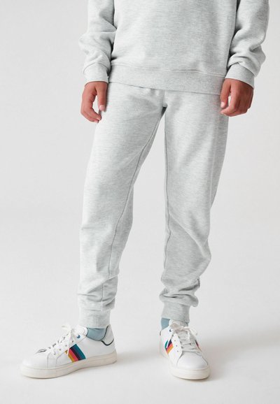 Pilkos sportinės kelnės su elastinėmis apykaklėmis ir juosmeniu; minkšta tekstūra su subtiliais siuvimo akcentais. Suderinta su baltais sportbatiais su vaivorykštės akcentais.