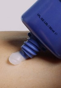 Bouteille violette distribuant une lotion épaisse et translucide sur une surface de peau claire, dotée d'un bouchon vissé et d'une zone de pression texturée.