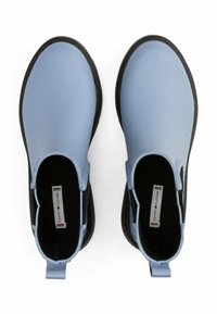 Bottines en caoutchouc bleu clair avec des panneaux élastiques noirs sur les côtés et des languettes de traction. Texture lisse avec un bout arrondi et une semelle plate.