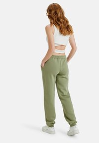 Olijfgroene sweatpants met een elastische tailleband, zijzakken en geribde manchetten. Gecombineerd met een witte, cropped tanktop. Glad textuur van de stof.