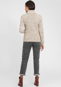 Beige gebreid sweater met een hoge kraag, geribde zoom en manchetten, gecombineerd met opgerolde grijze broeken en bruine haklaarzen.