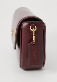 Burgunderfarbene Leder-Handtasche mit glatter Textur, rundem Klappen-Design und goldenen Beschlägen. Verfügt über ein Etikett mit geprägt Markenlogo.