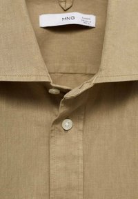 Beige linned skjorte med klassisk krave, der har en knapstolpe og to knapper, glat tekstur og synlige syningsdetaljer.