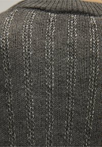 Tissu en tricot gris avec des accents de fil argenté, présentant des rayures verticales et une surface texturée, affichant une apparence douce et luxueuse.