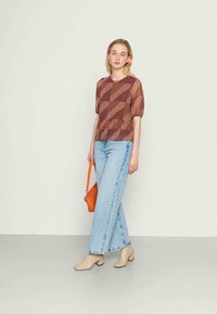 Blusa castanha com padrão e mangas curtas bufantes, combinada com jeans de perna larga de um azul claro. Acessórios incluem uma bolsa laranja e botas de salto beiges.