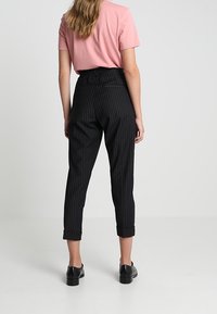 Svart och vit randiga, hög midja byxor med uppvikta ärmar, tillverkade av ett slätt tyg. Kombineras med en kort rosa skjorta och svarta skor.