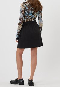 Jupe noire au toucher doux, taille élastique, complétée par un haut à manches longues en voile à motifs floraux avec des tons de bleu et de marron.