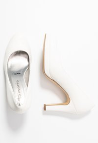 Bílé dámské boty na vysokém podpatku s kulatou špičkou a metalickými stříbrnými stélkami, zobrazené z vrchu a z boku na bílém pozadí.