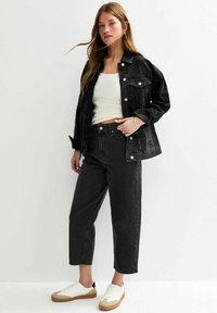 Veste en denim noire avec de gros boutons, associée à un jean noir et des baskets blanches. L'ensemble comprend un débardeur blanc ajusté.