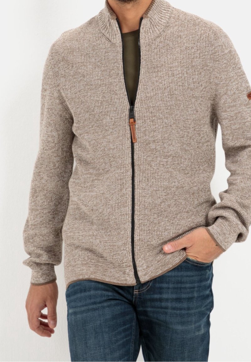 Beige Zip-Up-Cardigan aus strukturiertem Stoff mit hohem Kragen und schwarzem Reißverschluss, mit Handgelenksbündchen und Seitentaschen.