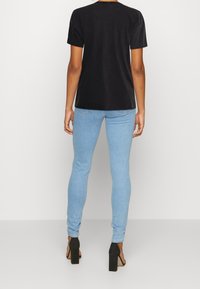 Camiseta negra de manga corta con un corte relajado, combinada con jeans ajustados de color azul claro. Zapatos negros de tacón grueso añaden altura.