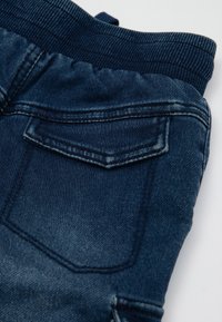 Jogger in denim con una lavatura blu scuro, caratterizzati da una vita a costine e una singola tasca posteriore con un dettaglio a patta cucita.