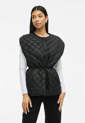 Chaleco acolchado negro con cuello redondeado, cierre de botones en la parte delantera y cintura ajustable con cordón. Presenta amplios huecos para los brazos y un diseño minimalista.