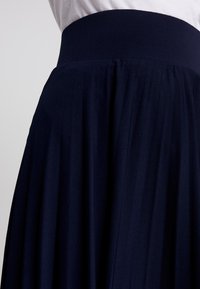 Marineblauer, plissierter Rock mit einem breiten Gummibund, gefertigt aus einem weichen Stoff, der sanft fällt, und einem klassischen, fließenden Design.