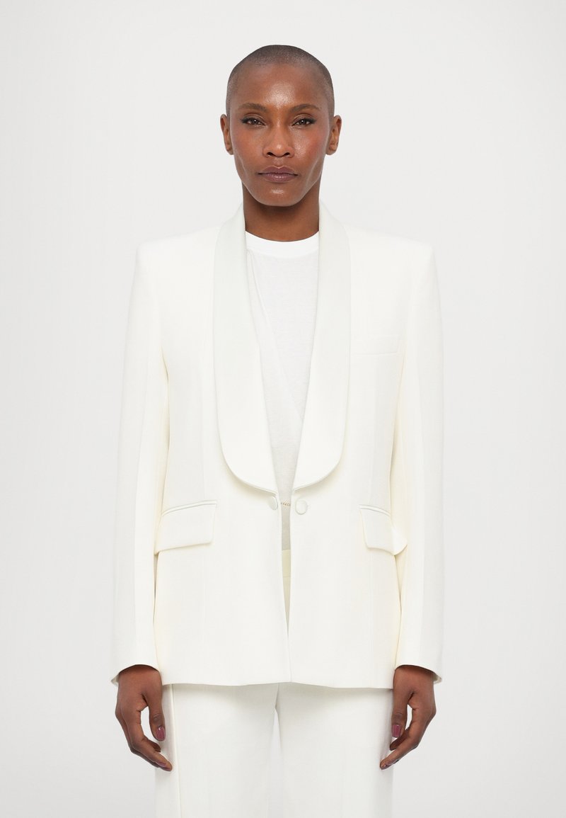 Witte op maat gemaakte blazer met een sjawlrevers, twee voorzakken en een gestructureerde silhoeet. Gladde stof met een ontspannen pasvorm.