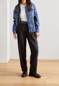 Džínová bunda s květinovou výšivkou, bílý tričko a černé široké kalhoty s jemným proužkem, doplněné černými platformovými mokasíny na dřevěné podlaze.