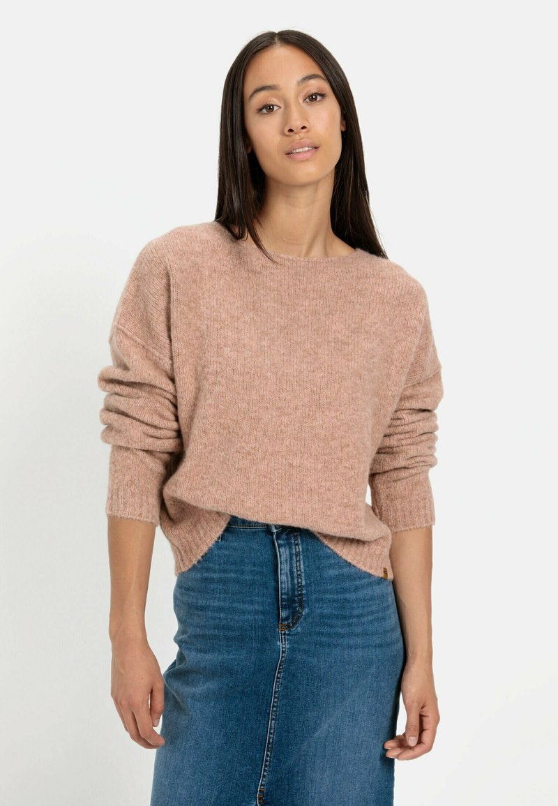 Lichtroze gebreide trui met een relaxte pasvorm en opgerolde mouwen, gecombineerd met een hoge taille blauwe denim rok. Zachte textuur, minimale details.