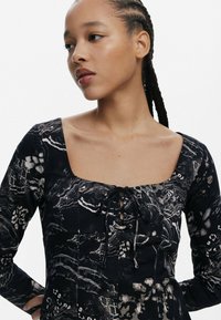 Sort langærmet kjole med firkantet udskæring, der har en snørret front og et detaljeret blomstermotiv samt abstrakte mønstre i grå nuancer.