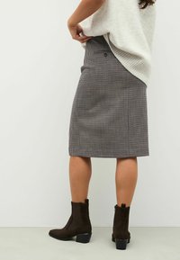 Fustă până la genunchi, cu un model tartan, realizată dintr-un material texturat. Asortată cu bocanci de gleznă din suede maroniu, cu un toc gros.
