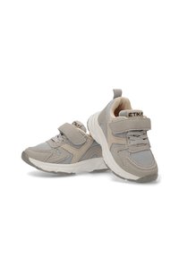 Zapatillas infantiles en gris y beige con detalles de malla y gamuza, correa de gancho y bucle y suelas blancas, posicionadas con un zapato apoyado sobre el otro.