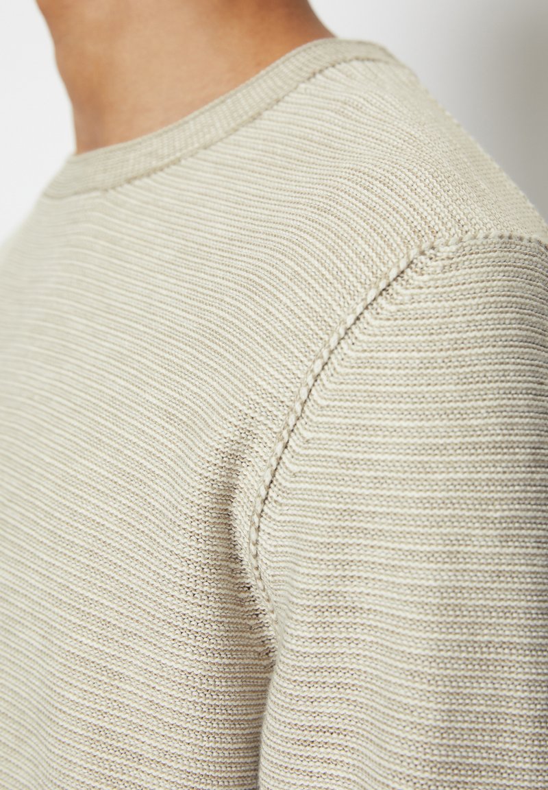 Beżowy sweter dzianinowy z teksturowanym prążkowanym wzorem, okrągłym dekoltem i subtelnym detalem przeszycia na ramieniu.
