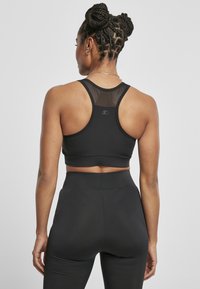 Čierny športový podprsenka s sieťovinovými detailmi, so strihom racerback. Pár čiernych legín s vysokým pásom, hladkou textúrou a priliehavým siluetou.