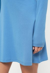 Φόρεμα μακρυμάνικο σε ανοιχτό μπλε χρώμα, κατασκευασμένο από απαλό ύφασμα. Διαθέτει ροή σχεδιασμού με στρογγυλεμένη γραμμή στο τελείωμα και ριμπ μανσέτες στα μανίκια.