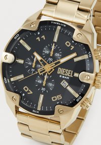 Arany Diesel karóra fekete számlappal, arany órajelzőkkel, három segédszámlappal, dátumablakkal 4 óránál és arany színű fém szíjjal.