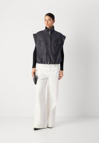Mørk denim utenermed to brystlommer og trykknapper, kombinert med høytlivede hvite bukser og en svart clutch.
