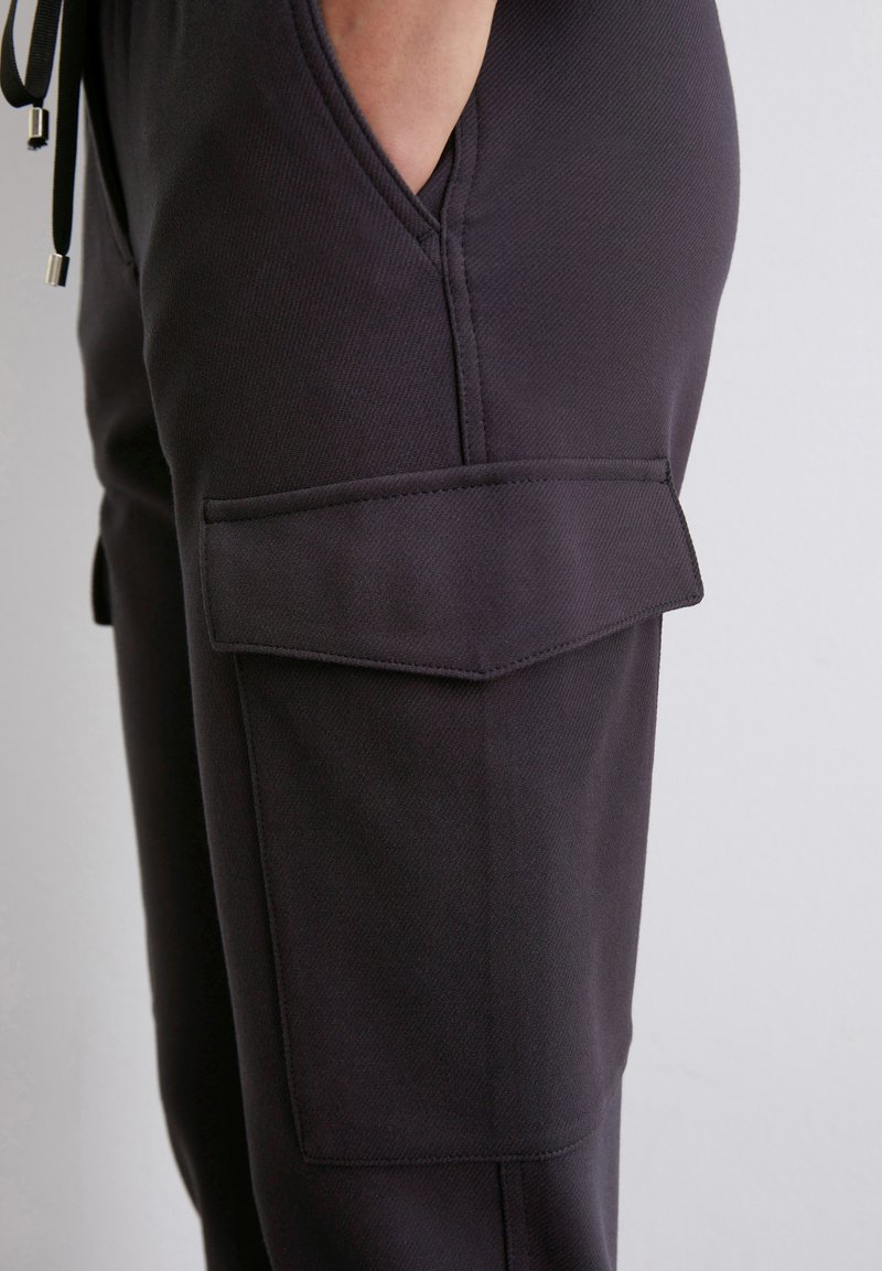 Czarne spodnie cargo z teksturowanej tkaniny, z bocznymi kieszeniami zamykanymi na klapki oraz regulowanym sznurkiem w pasie.