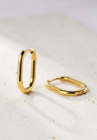 Orecchini a cerchio in oro a forma ovale allungata, con una texture liscia e una finitura lucida, dotati di un semplice design della chiusura.