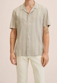 Camicetta a maniche corte con bottoni di colore beige chiaro, con sottili righe verticali gialle e grigie. Tessuto morbido con una vestibilità rilassata e colletto aperto.