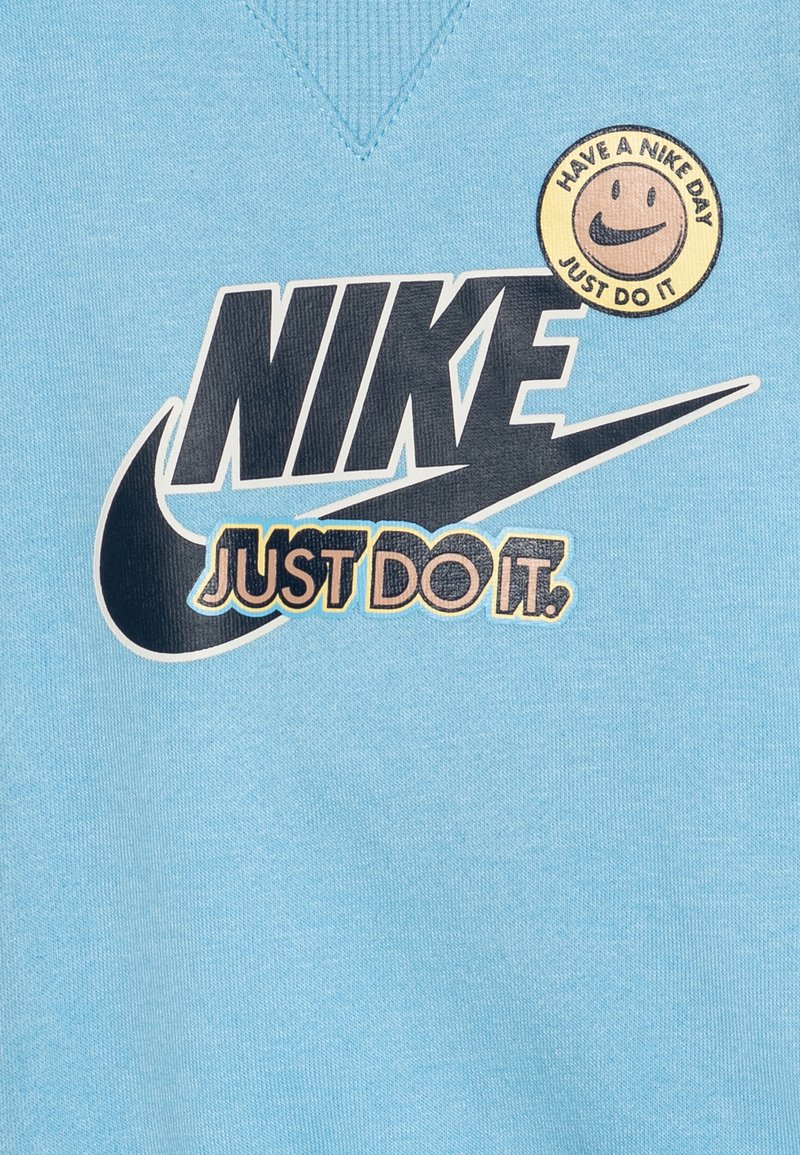 Jasnoniebieska bluza z dużym czarnym logo Nike i napisem "Just Do It", z okrągłą przywieszką z uśmiechem, na której jest napis "Have a Nike Day".