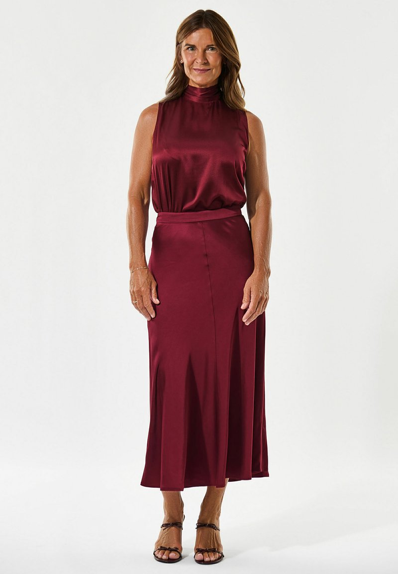 Bordo sateninė suknelė su aukštu kaklu, sruvenančia sijonu ir prigludusia juosmens dalimi. Yra skeltukas judėjimui. Poruojama su diržinėmis šlepetėmis.