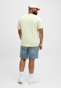 Lys gul kortærmet t-shirt parret med denim shorts. Hvide sneakers med hvide sokker. Kasket med orange accenter. Enkel og afslappet look.